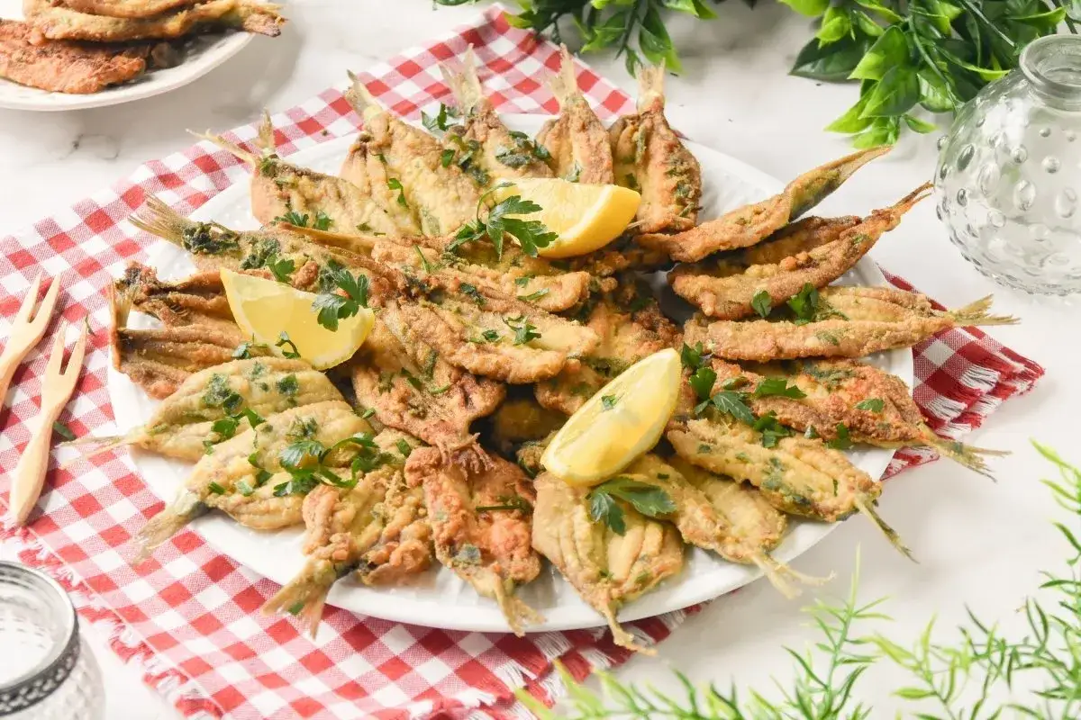 Plato de boquerones en adobo, crujientes y dorados, adornados con perejil fresco y gajos de lim&oacute;n.