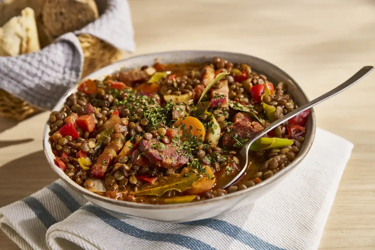Un plato humeante de lentejas estofadas con verduras y chorizo, la aut&eacute;ntica lentejas receta de la abuela, servido en un cuenco r&uacute;stico.