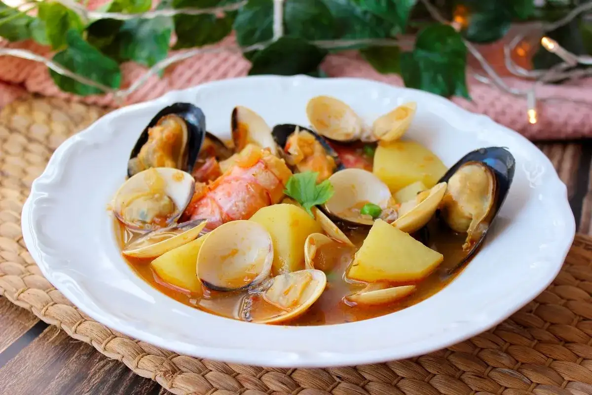 Delicioso plato de patatas a la marinera con mejillones, almejas y trozos de langosta en una salsa sabrosa.