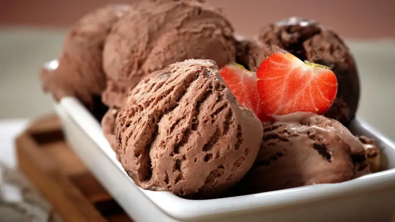 Un taz&oacute;n blanco lleno de cremoso helado de chocolate, decorado con rodajas de fresa fresca.