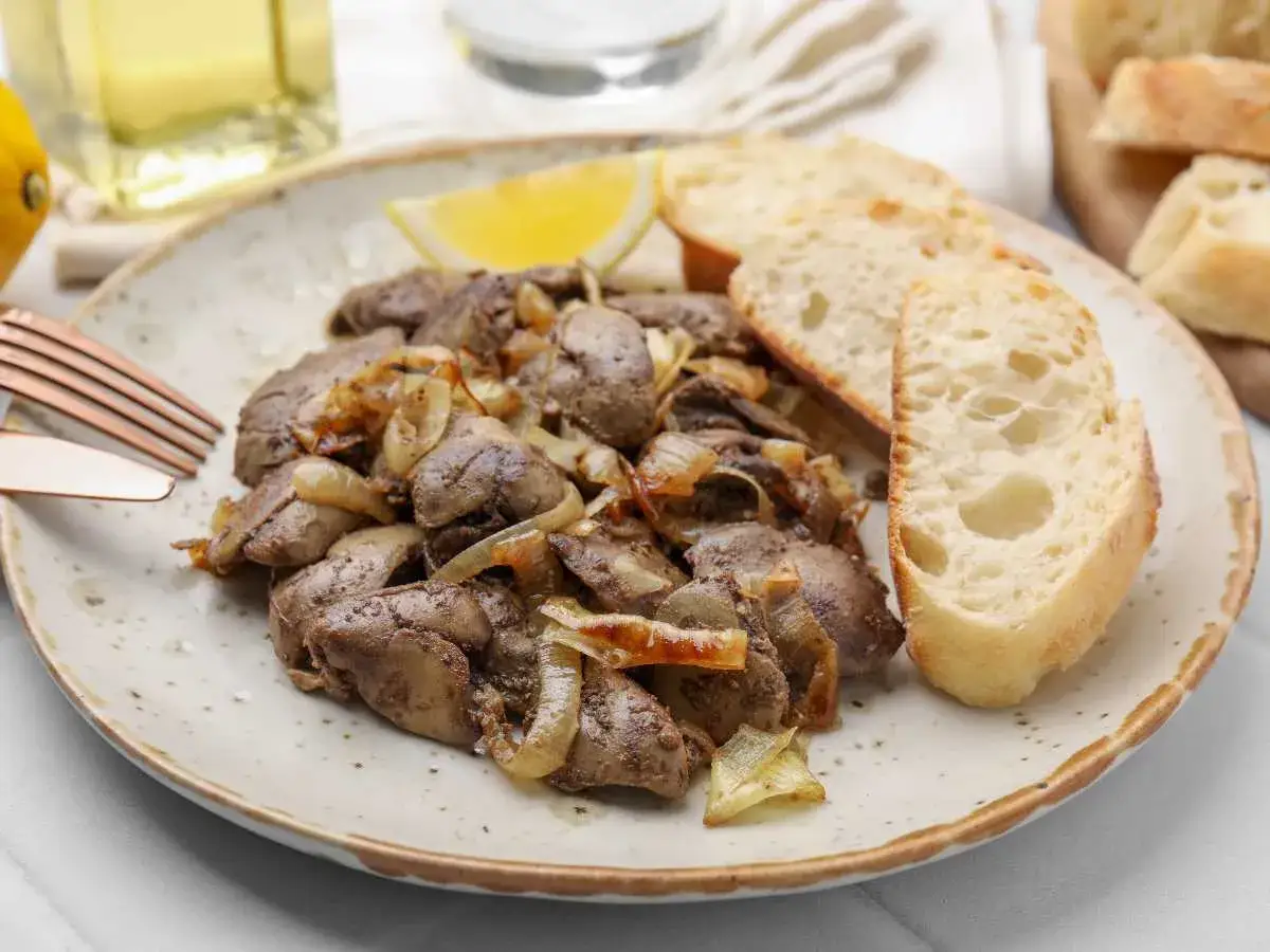 Sabrosos higaditos de pollo salteados con cebolla, acompa&ntilde;ados de pan r&uacute;stico y una rodaja de lim&oacute;n.