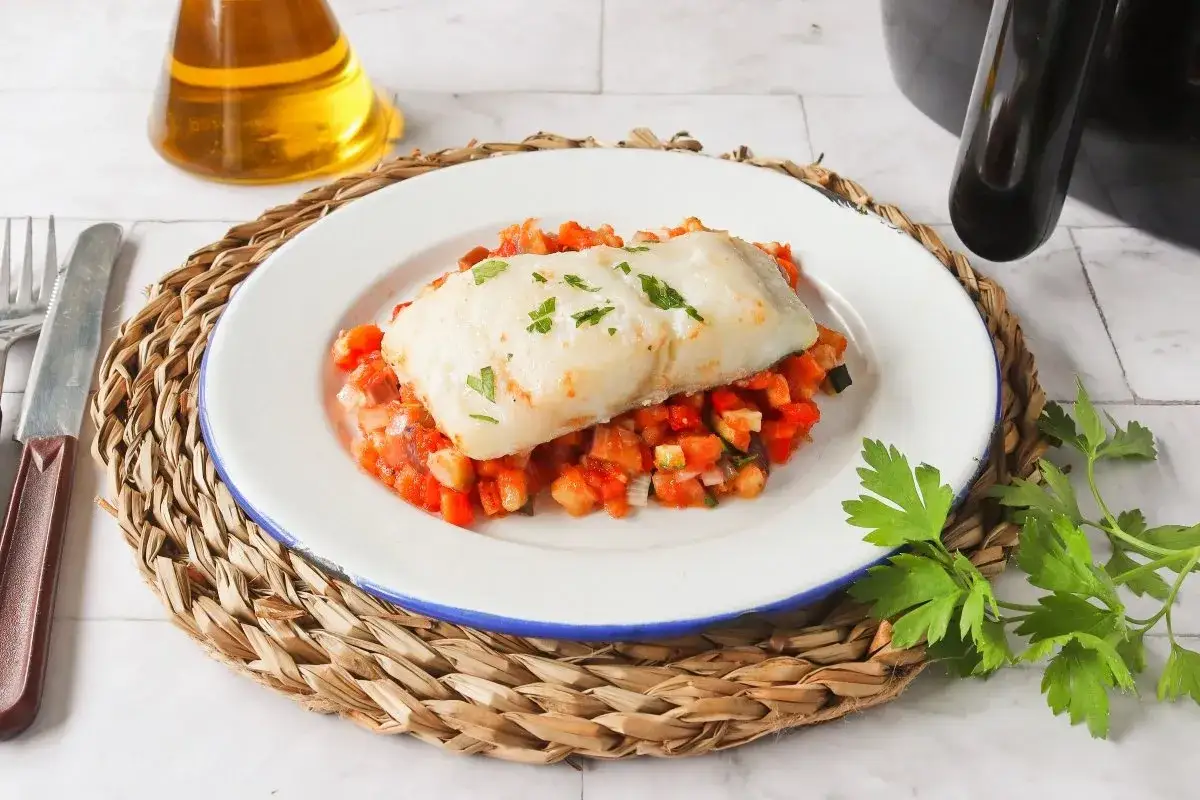Filete de bacalao jugoso sobre cama de verduras, preparado en airfryer. Un plato saludable y delicioso.
