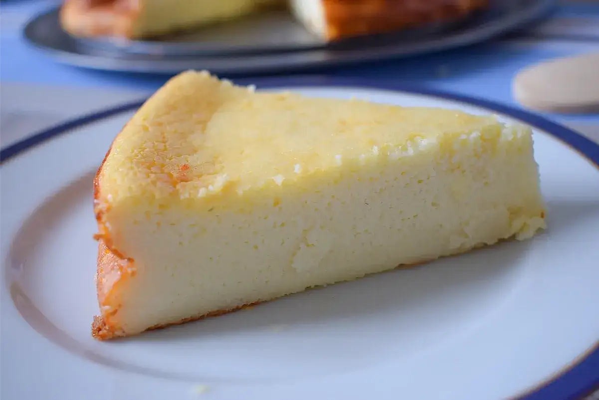 Una rebanada de tarta de queso cremosa y esponjosa, con un borde dorado, servida en un plato blanco.