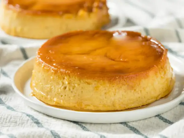 Delicioso flan de plátano con caramelo dorado, servido en un plato blanco sobre un mantel a rayas.
