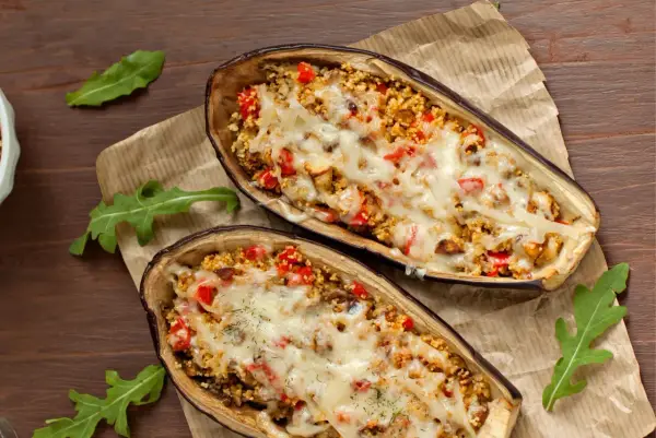 Dos mitades de berenjenas rellenas con cuscús, pimientos y queso derretido, cocinadas en airfryer.
