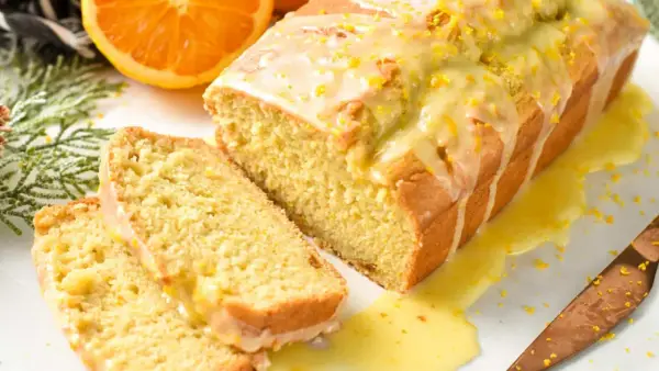 Un delicioso bizcocho de naranja, cubierto con glaseado y ralladura, con dos rebanadas cortadas.