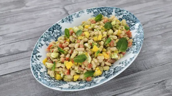 Deliciosa ensalada de alubias con trozos de tomate, mango y huevo, decorada con hojas de menta fresca.