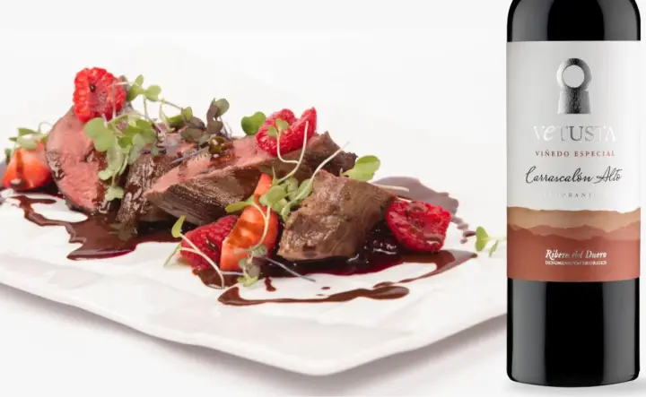 Filete de ternera con fresas y frambuesas, bañado en salsa, junto a una botella de vino Vetusta de la **Ribera del Duero**.