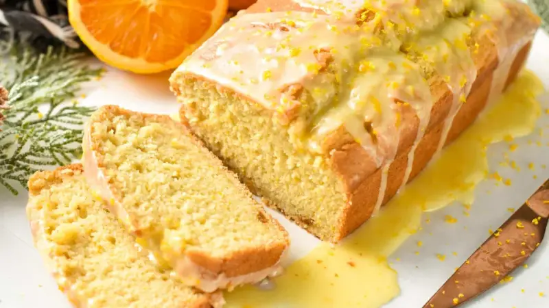 Un delicioso bizcocho de naranja, cubierto con glaseado y ralladura, con dos rebanadas cortadas.