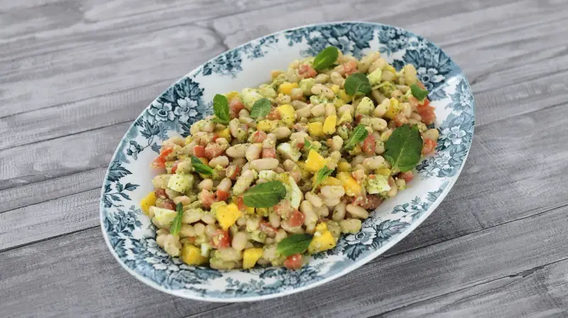 Deliciosa ensalada de alubias con trozos de tomate, mango y huevo, decorada con hojas de menta fresca.